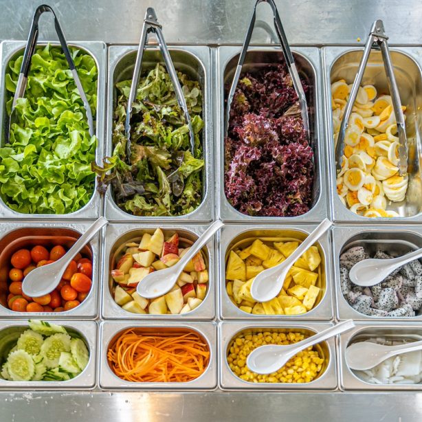 Top view of salad bar with various types of vegetables and fruits including lettuce, tomato, corn, egg, watermelon, carrot, cucumber, and more